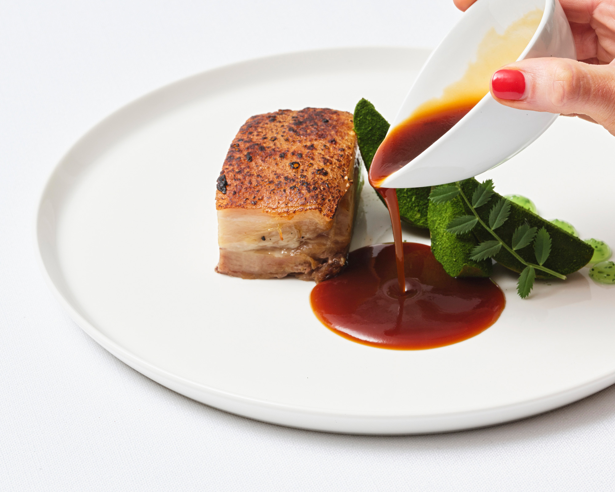 A formal plated boardroom main course of roasted pork belly with jus and green vegetables