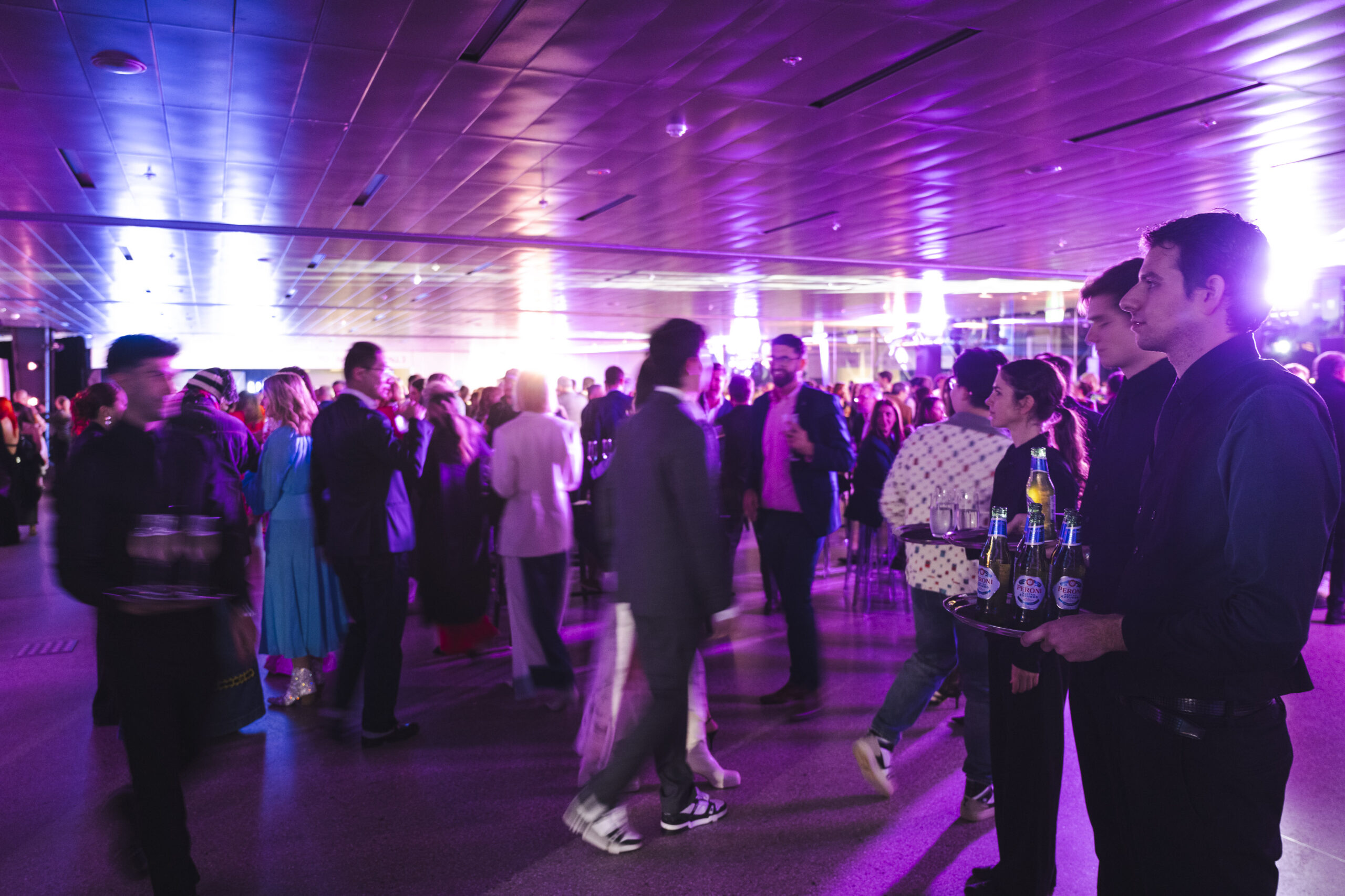 Networking event at a conference held in Sydney. The crowd gathers and mingles while waiters with trays of drinks serve them.