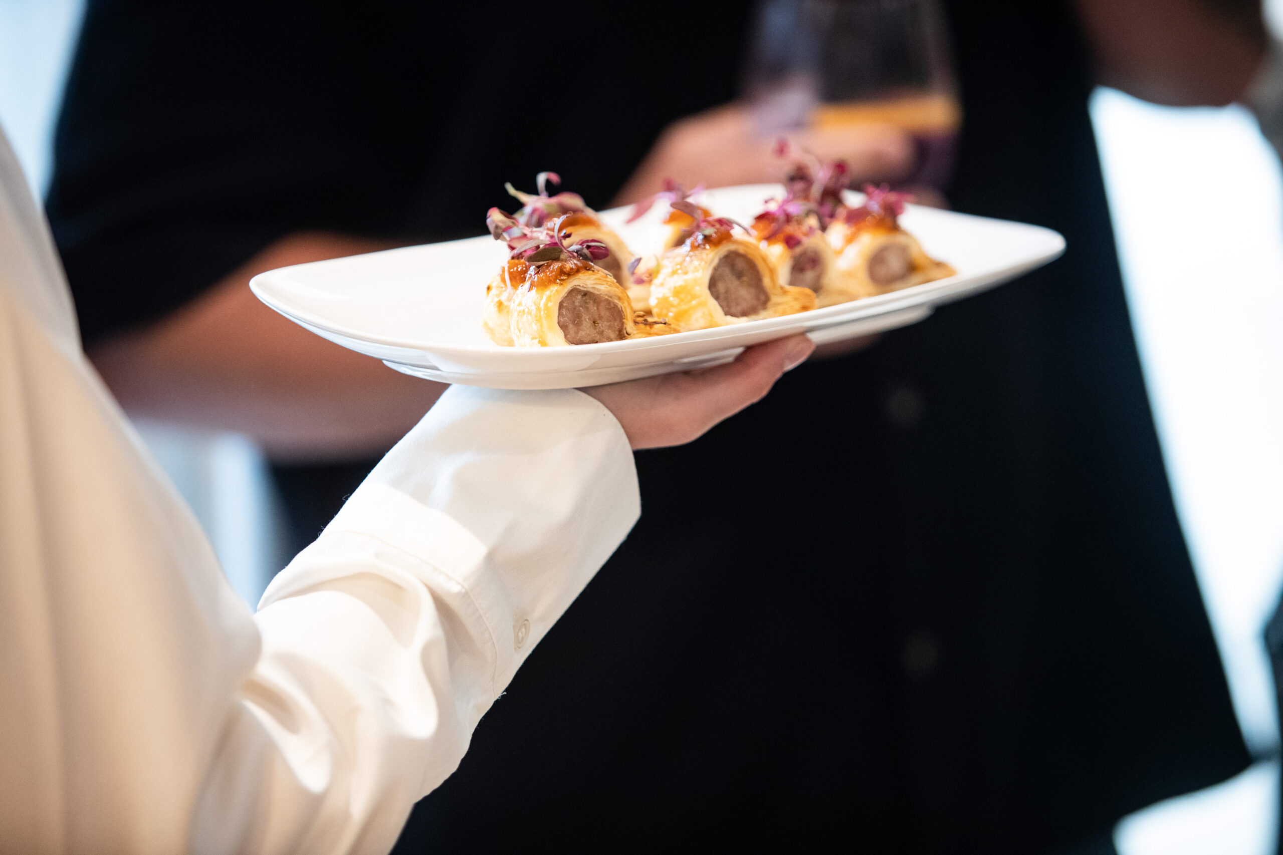 Waiter carrying a platter of miniature pork and fennel sausage rolls to guests