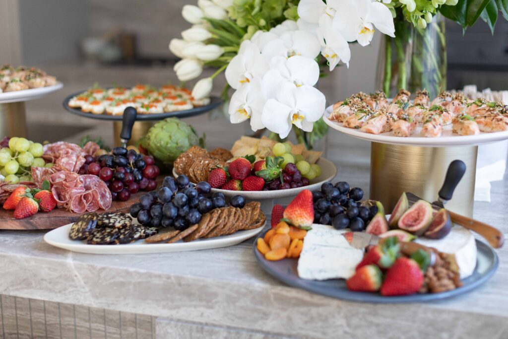 grazing table adorned with finger foods, artisan cheeses, deli meats, antipasto, crackers and fresh florals