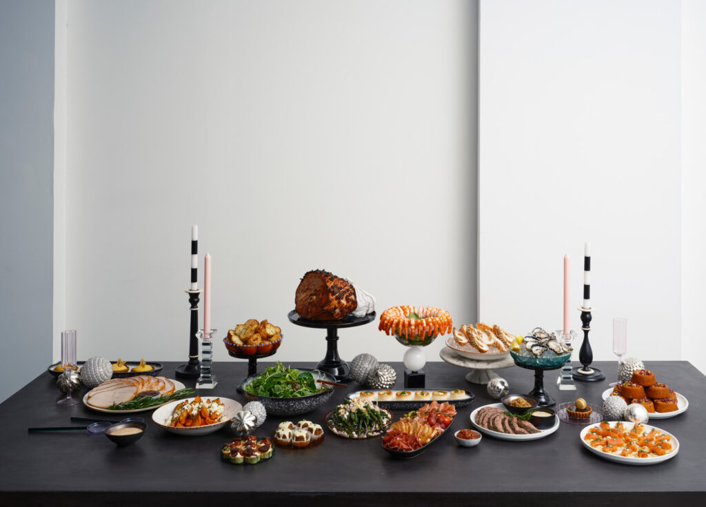 An impressive Christmas buffet spread by The Blonde Butler, delivered ready to go with ham, turkey, sides and desserts, set up on a black dining table.