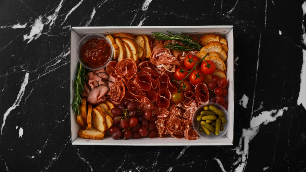 Charcuterie box delivered for convenience by Boxed by Blonde Butler, which includes prosciutto, crackers, suppress, salami and bresaola with cornichons and relish.